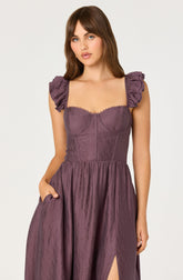 A woman is wearing a mauve-colored dress with short, ruffled sleeves and a fitted bodice featuring stitched detailing. The skirt is full and gathered, with a slit on one side. The fabric has a textured, slightly shiny appearance.